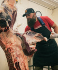Seth removing a section of meat from a hanging animal carcass 