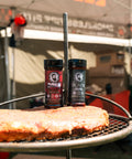 Two bottles of spice on a grill with a blurred background