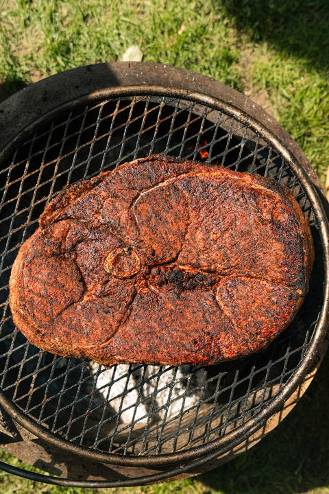 Rust-covered steak on a grill with grass in the background