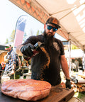 Man seasoning a large piece of meat at an outdoor event.