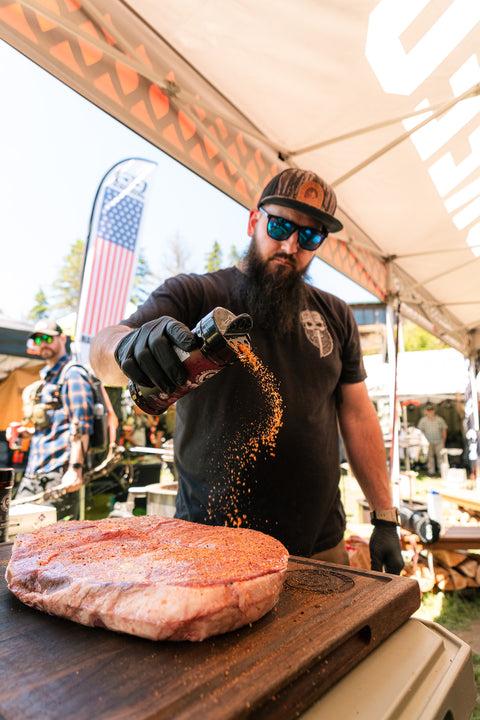 Man seasoning a large piece of meat at an outdoor event.