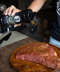 Person seasoning raw steaks with a spice blend on a wooden cutting board.