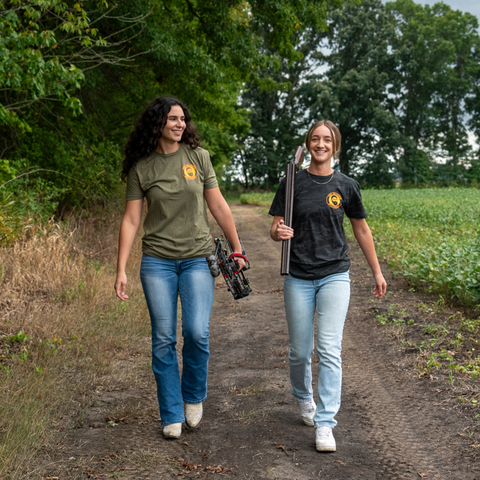 Women walking with a bow and gun wearing bearded butcher apparel.