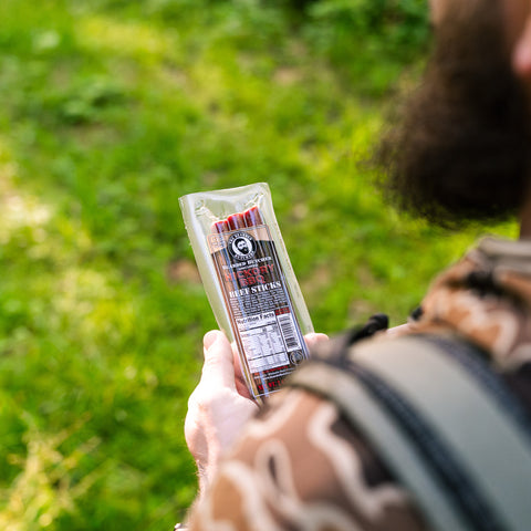 Person holding a package of beef sticks outdoors with green grass in the background