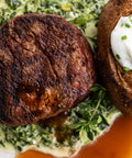 Close-up of a cooked steak with a baked potato and green sauce on a plate.