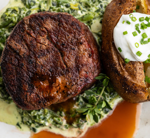 Close-up of a cooked steak with a baked potato and green sauce on a plate.