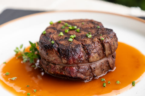 Grilled steak with a red sauce on a white plate