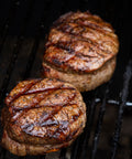 Two grilled steaks on a barbecue grill with visible grill marks.