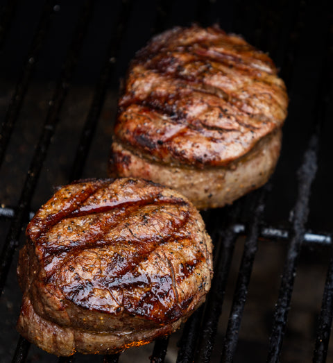 Two grilled steaks on a barbecue grill with visible grill marks.