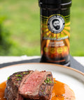 Sliced steak with sauce on a plate with a bottle of seasoning in the background.