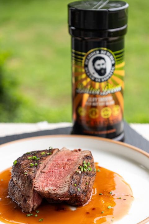 Sliced steak with sauce on a plate with a bottle of seasoning in the background.