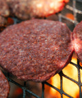 Hamburger patties cooking on a grill with flames