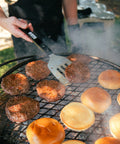 Person grilling hamburgers and buns on a barbecue grill.
