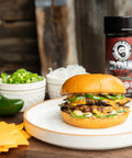 Burger on a plate with jalapeños, cheese, and a shaker of Bearded Butcher Bold Blend on a wooden table.
