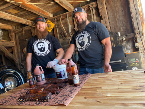 Scott and Seth wearing Bearded Butcher Blend T-Shirts at table with Sauces, Ribs, and Seasonings
